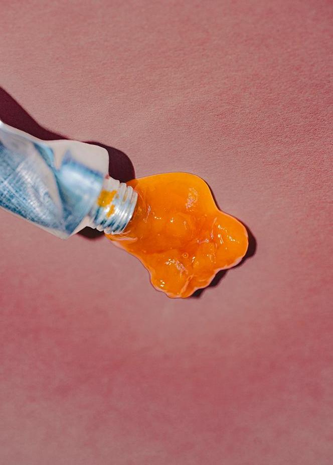 A tube of orange paint or preserve squeezed onto a pink background